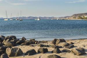 malecón de la paz junto ao mar de cortes com pedras na praia e vista da cidade com navios no mar foto