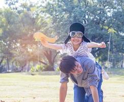 pai e filho jogando aviões de papel no parque. o filho está nas costas do pai. foto