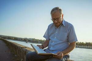 Senior homem lendo uma livro lado de fora foto