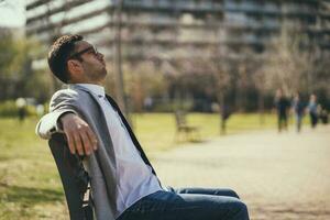 uma homem de negocios sentado em uma parque Banco foto