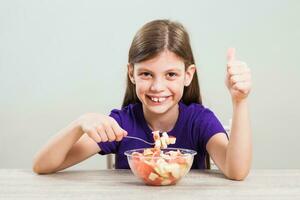 uma menina comendo uma fruta salada foto