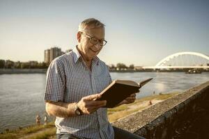 Senior homem lendo uma livro lado de fora foto