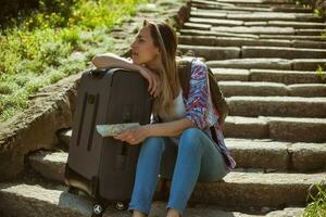 jovem turista mulher sentado de a escadas com uma mala de viagem foto