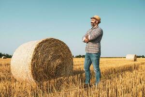 uma agricultor é em pé ao lado fardos do feno foto