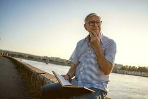 Senior homem lendo uma livro lado de fora foto