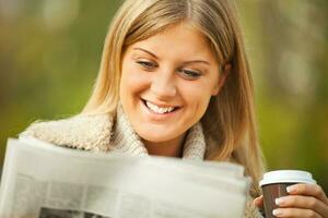 uma mulher tendo café dentro a parque e lendo uma jornal foto