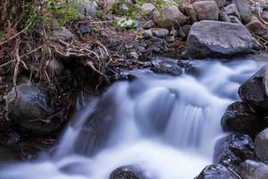 córrego de água pura com fluxo suave em terreno montanhoso rochoso na floresta kakopetria em troodos chipre foto