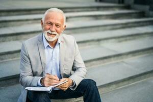 uma Senior homem de negocios escrevendo dentro uma caderno foto