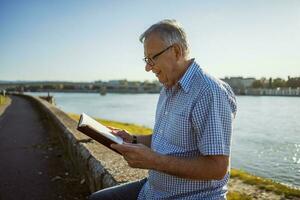 Senior homem lendo uma livro lado de fora foto
