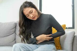 flatulência ásia jovem mulher, menina mão dentro estômago dor, Sofra a partir de Comida envenenamento, abdominal dor e cólon problema, gastrite ou diarréia. paciente barriga, abdômen ou inflamação, conceito. foto