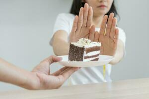 dieta, dieta pouco saudável ásia jovem mulher mão dentro empurrar fora, rejeitando comer chocolate bolo ou doce gosto, brigando para manter isto a partir de obtendo gordo quando pessoa trazer para meu. saudável, nutrição do peso perda foto