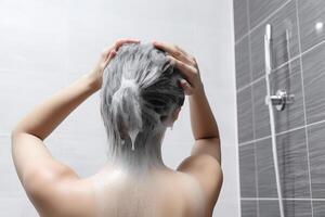 mulher lavando cabelo com xampu e chuveiro dentro a banheiro. ai gerado foto