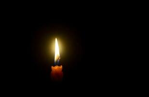 uma solteiro queimando vela chama ou luz brilhando em espiral laranja vela em Preto ou Sombrio fundo em mesa dentro Igreja para Natal, velório ou memorial serviço com cópia de espaço foto