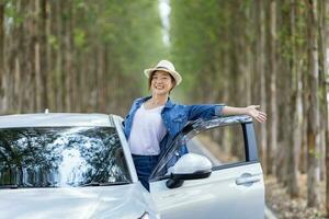 ásia turista mulher é desfrutando em a viagem enquanto tendo período de férias às a nacional parque dirigindo baixa a estrada com coluna do árvore para viagem e aventura conceito foto