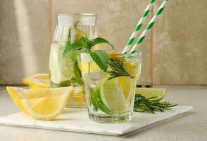 limonada dentro uma transparente vidro com limão, Lima, alecrim raminhos e hortelã folhas em uma branco fundo foto