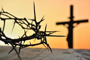 coroa de espinhos de Jesus Cristo contra a silhueta da cruz católica no fundo do sol foto
