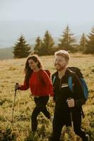 jovem casal caminhando com mochila sobre verde colinas foto