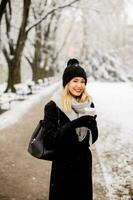 jovem mulher dentro caloroso roupas desfrutando dentro neve com Leve embora café copo foto