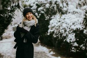 jovem mulher dentro caloroso roupas desfrutando dentro neve com Leve embora café copo foto