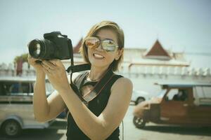 mulher cheio de dentes sorridente com felicidade segurando dslr Câmera em pé dentro Ayutthaya Tailândia foto