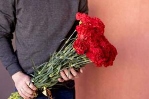 uma ampla ramalhete do vermelho cravos com uma Preto fita dentro a mãos do uma homem foto