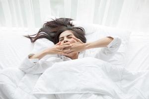 mulher bocejando na cama branca foto