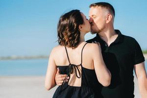 jovem casal um cara com uma garota em roupas pretas está andando na areia branca foto