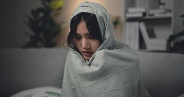 ásia jovem mulher sentado debaixo cobertor com sofrimento a partir de frio e gripe às casa foto