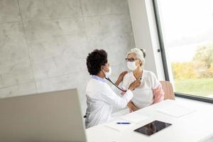 médico examinando mulher madura com máscara foto