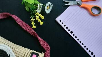 Rosa caderno, tesoura, flores, e saco estão em uma Preto fundo Como a elegante fundo. Educação conceito, o negócio conceito, em branco documento, em branco papel. foto