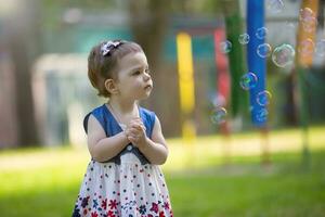 a pequeno menina parece às Sabonete bolhas. bonita bebê em uma verão andar. foto