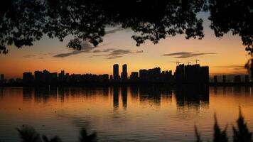 a lindo pôr do sol Visão com a edifícios' silhueta e laranja cor céu espelhado dentro a pacífico lago dentro a cidade foto