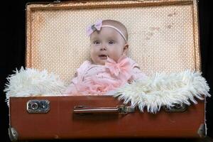 uma pequeno bebê senta dentro uma retro mala de viagem e sorri. bonita bebê. foto