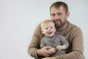 em uma cinzento fundo, uma retrato do uma pai e uma pequeno um ano de idade sorridente filho. foto