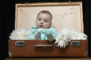 uma pequeno criança senta dentro uma retro mala de viagem e parece às a Câmera. bonita bebê. foto