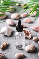 conta-gotas de óleo essencial para cuidados com a pele em frasco de vidro próximo a conchas e seixos foto
