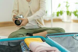 viajante. fêmea é preparando uma Câmera para viagem e fotografia. mulheres estão preparar roupas e pessoal pertences. pacote seu bagagem antes viagem. feriado, período de férias tempo, grandes fim de semana, verão foto