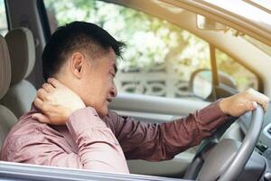 ásia homem sente doeu dele pescoço e ombros durante dele grandes dirigindo dentro carro. conceito ferida, dor ou cansado a partir de dirigindo. inseguro dirigindo durante anormal sintomas. transporte, assistência médica. saúde problema foto