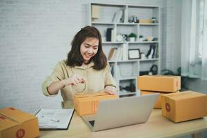 ásia Entrega mulher freelance sorridente e embalagem caixa do produtos trabalhando às casa , verificação Lista parcela caixas para enviando ou transmitindo parcelas de correspondência. foto