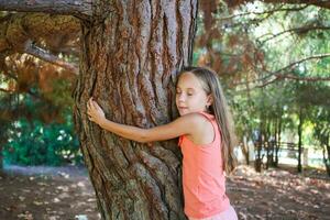 menina abraçando árvore dentro parque. foto