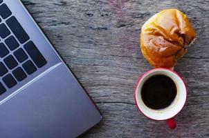 xícara de café vermelha e pão saboroso com laptop na mesa de madeira foto