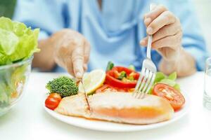 ásia idosos mulher paciente comendo salmão estaca e vegetal salada para saudável Comida dentro hospital. foto