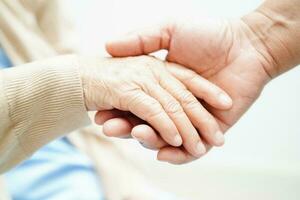 cuidador de mãos dadas paciente idosa asiática, ajuda e cuidados no hospital. foto
