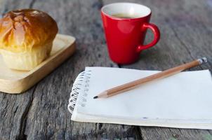 close up de lápis com bloco de notas e pão, copo vermelho no fundo da mesa de madeira foto