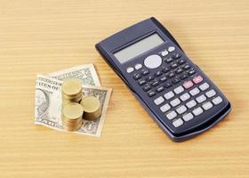 calculadora e moedas de dólar empilhadas na mesa de madeira foto