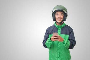 retrato do ásia conectados Táxi motorista vestindo verde Jaqueta e capacete segurando uma Móvel telefone e sorridente. publicidade conceito. isolado imagem em branco fundo foto