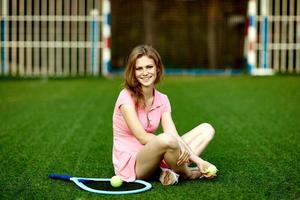 menina sentada no gramado de um campo de tênis com uma raquete de tênis foto