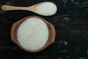 arroz de jasmim em uma panela de barro e uma concha de madeira isolada em um fundo preto foto