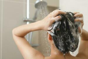 mulher levando chuveiro e lavando cabelo com xampu foto