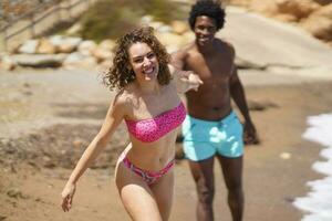 alegre diverso casal segurando mãos enquanto corrida em de praia foto